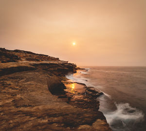 Scenic view of rock formation by sea against sky during sunset