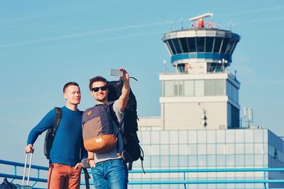 Man with friend taking selfie from mobile phone outside airport