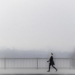 Man walking on railing against sky