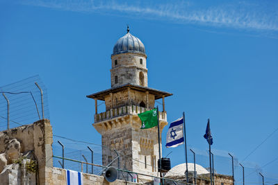 Israeli flag waving by historic building against blue sky