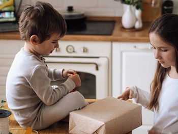 Brother and sister wrapping gift at home