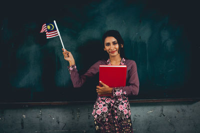 Teacher holding flag while standing against blackboard in classroom