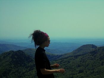 Side view of woman looking at mountains against sky