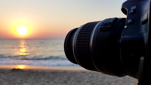 Close-up of camera on beach against sky during sunset