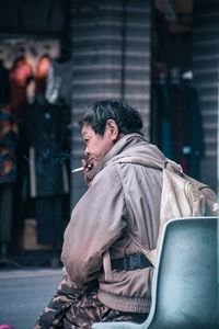 Side view of man smoking cigarette while sitting on chair