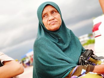 Low angle view of senior woman wearing hijab looking away against cloudy sky