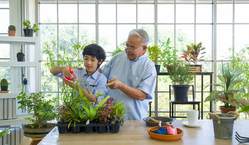 Grandfather looking at grandson watering plants in greenhouse