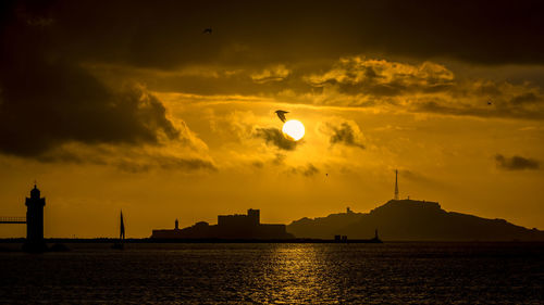 Silhouette buildings by sea against sky during sunset