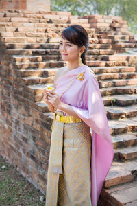 Side view of young woman standing against brick wall