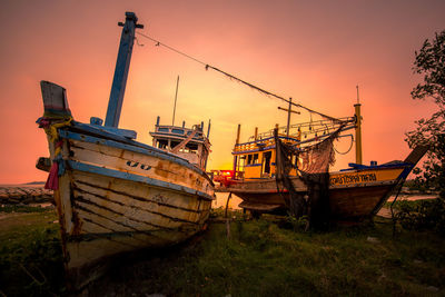 Abandoned boat moored on field against sky during sunset