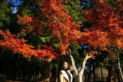 Portrait of woman standing by trees during autumn