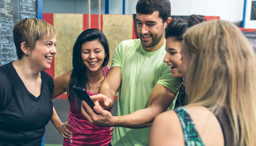 Smiling friends looking at smart phone while standing at gym