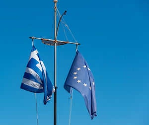 Low angle view of flags hanging against clear blue sky