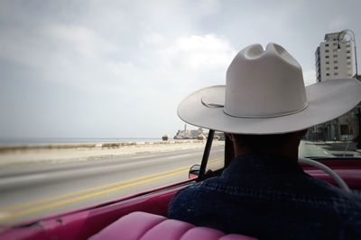 Rear view of man riding convertible car by sea against sky