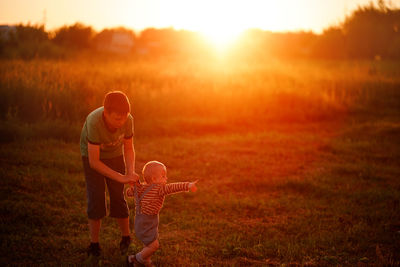 Boy playing with his brother on the grass at sunset