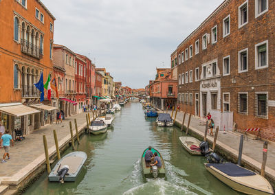 Boats in canal amidst buildings in city against sky