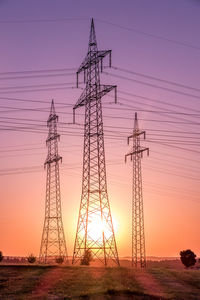 Low angle view of electricity pylon on field during sunset
