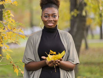 Portrait of smiling young woman standing against yellow flowering plants