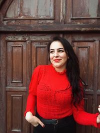 Portrait of smiling woman standing against door