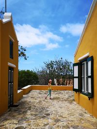 Woman walking by building against sky