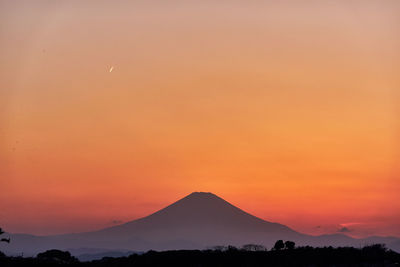 Scenic view of silhouette volcanic mountains against orange sky