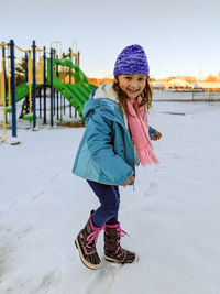 Portrait of happy girl playing on snow covered land