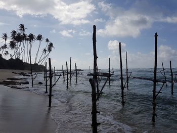 Wooden posts in sea against sky