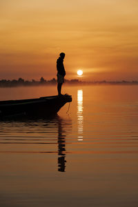 Silhouette man standing by sea against sky during sunset