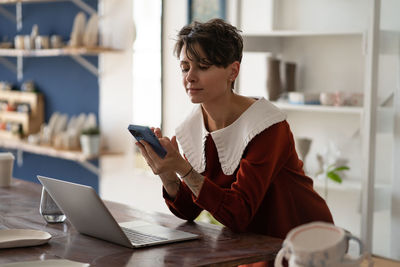 Georgian female ceramics artist holding mobile phone interacting with customers online.