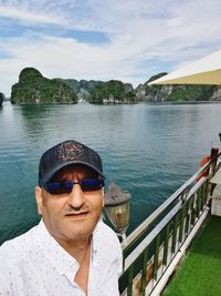 Portrait of smiling man at railing by river against sky