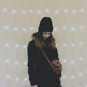 Young woman in warm clothing standing against illuminated lights