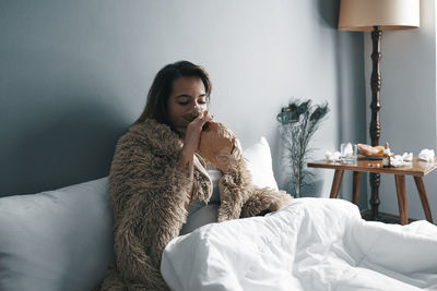 Young woman breathing in paper bag on bed at home