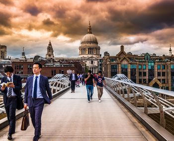 People in front of building against cloudy sky