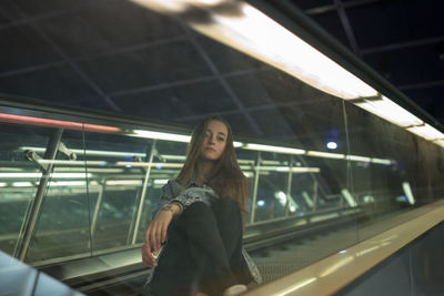 Portrait of young woman sitting on escalator seen through glass