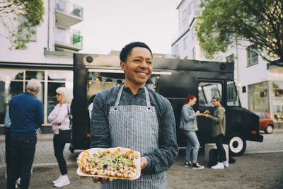 Smiling male owner with indian food plate looking away in city