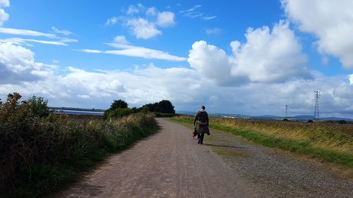 Rear view of young man walking on road against sky