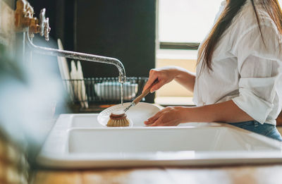 Midsection of woman cleaning dishes at home