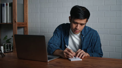 Young man using mobile phone while sitting on table