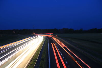 Light trails on road against clear blue sky at night