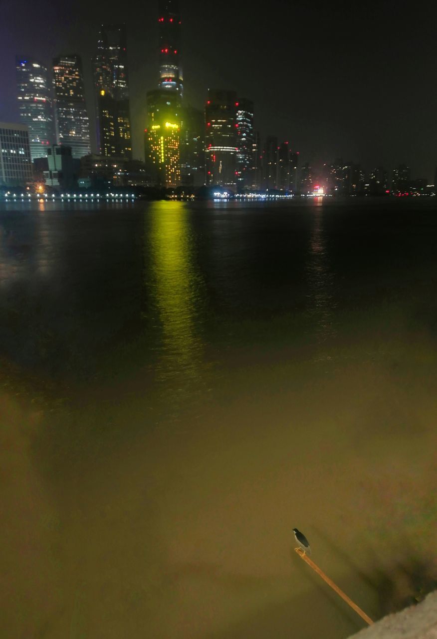 ILLUMINATED BUILDINGS BY RIVER AGAINST SKY AT NIGHT