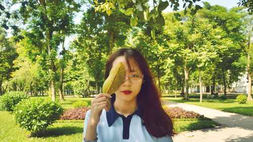 Portrait of beautiful young woman holding plants against trees