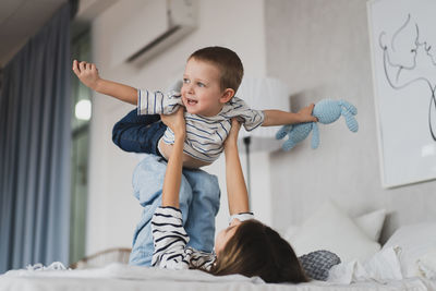 Boy playing with teddy bear while lying on bed at home