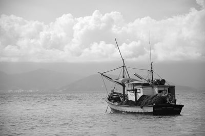 Fishing boat in sea against cloudy sky