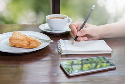 Close-up of hand holding coffee cup on table