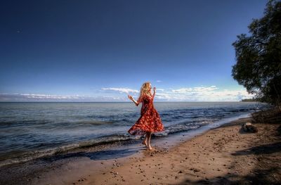 Woman dancing at beach against sky