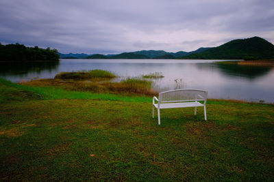 Empty chairs by lake against sky