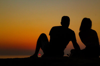 Silhouette people against orange sky during sunset