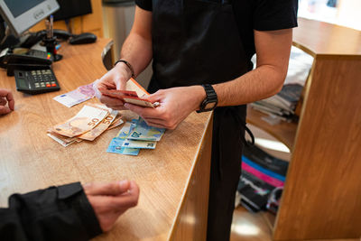 Unrecognizable salesman counting cash over counter for crop customer in modern store