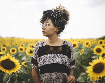 Beautiful young woman standing by flowers against sky