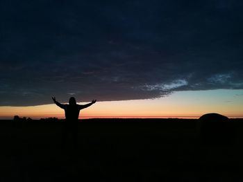 Silhouette man standing on field against sky during sunset